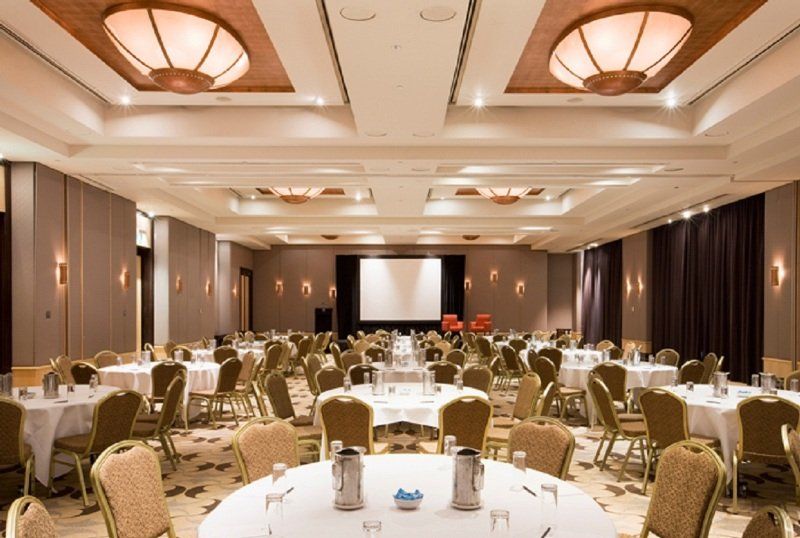 Amora Hotel Jamison Sydney Eksteriør bilde The photo shows a large banquet or conference room. There are several round tables arranged throughout the space, each covered with white tablecloths. The tables are set with water pitchers and glasses. In the center of the room, there is a projectio